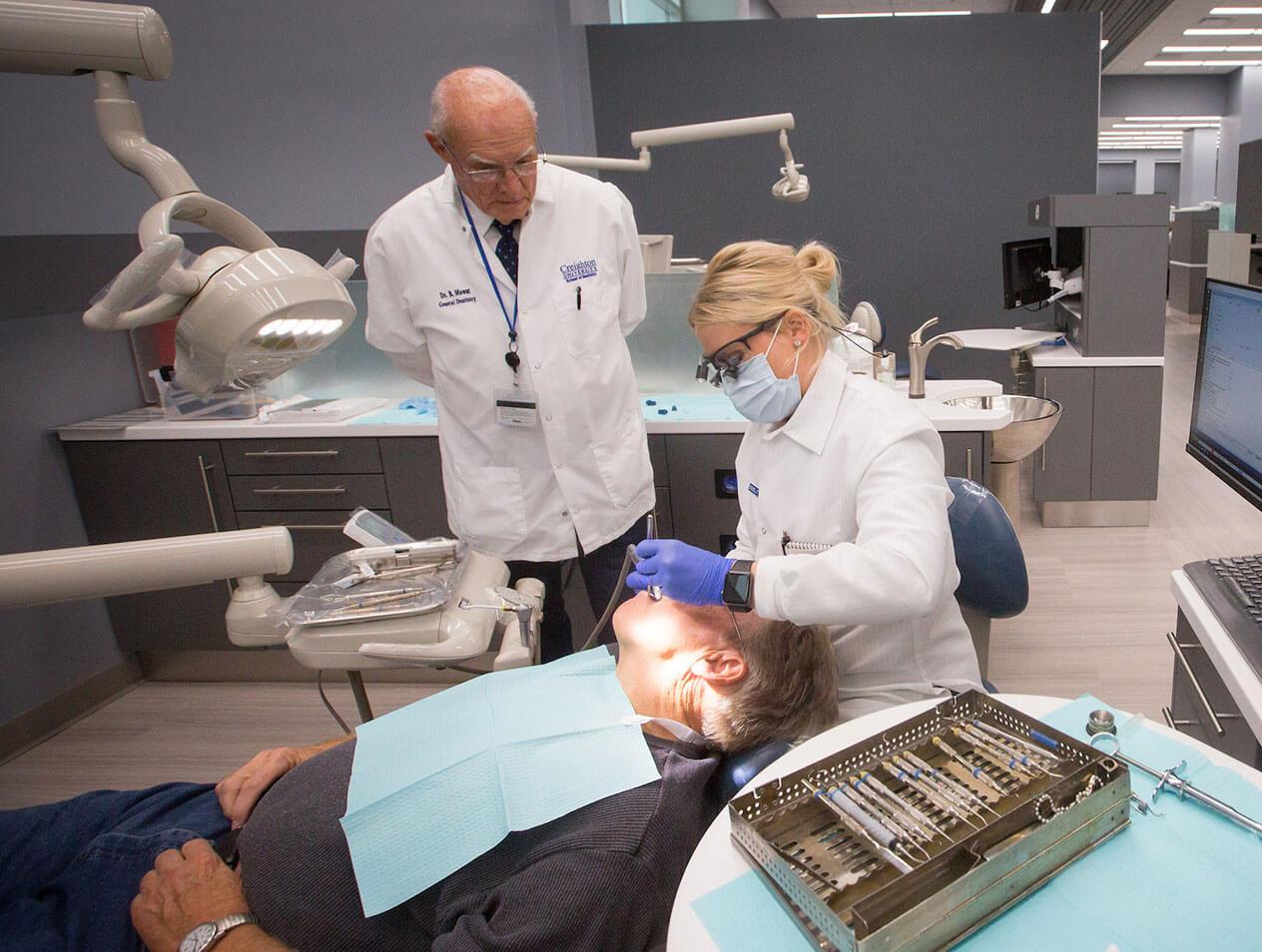 A dentist performs a procedure on a patient during a continuing education course while a professor looks on