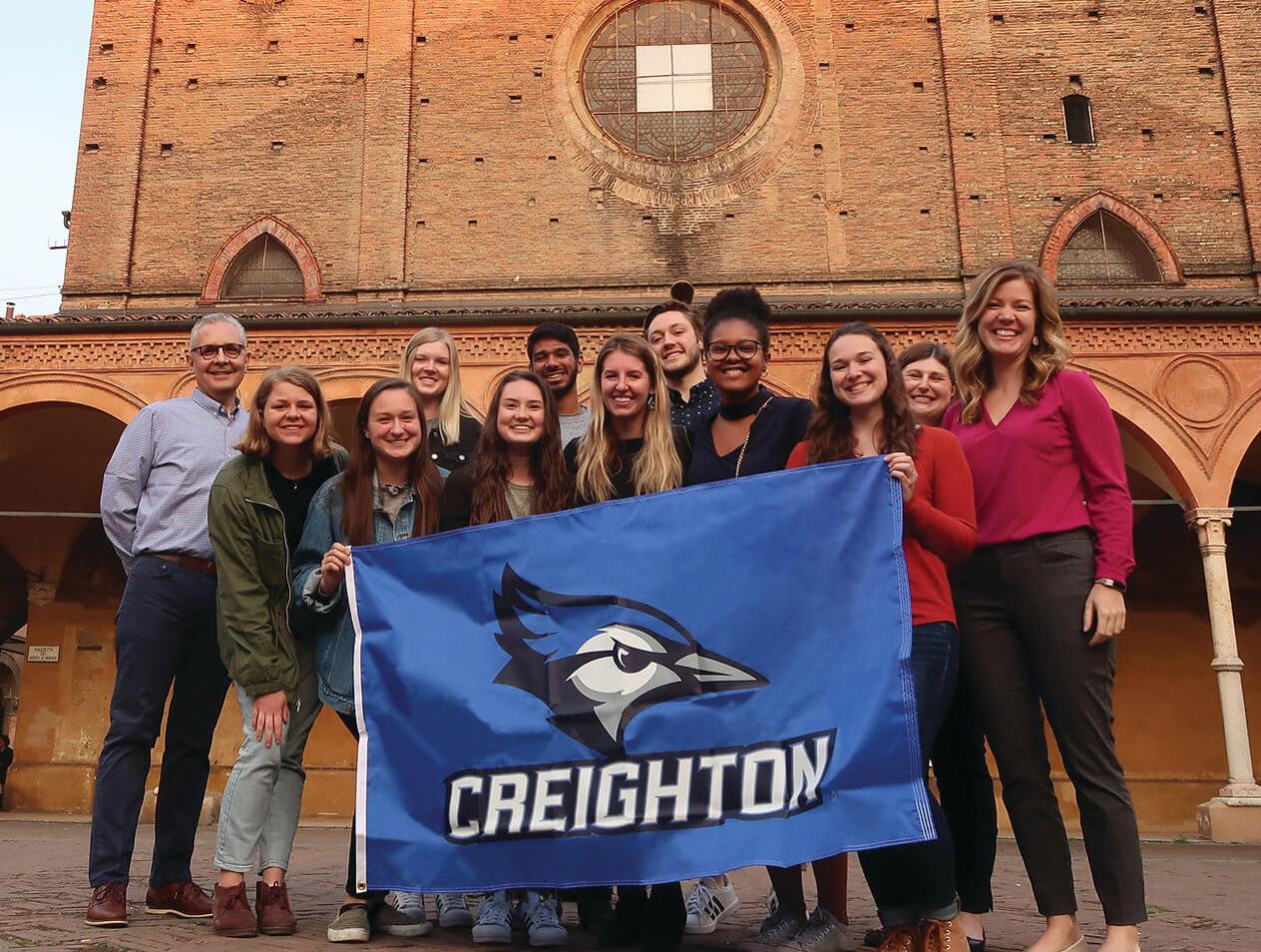 A group of Creighton students pose with a Creighton flag on an international trip