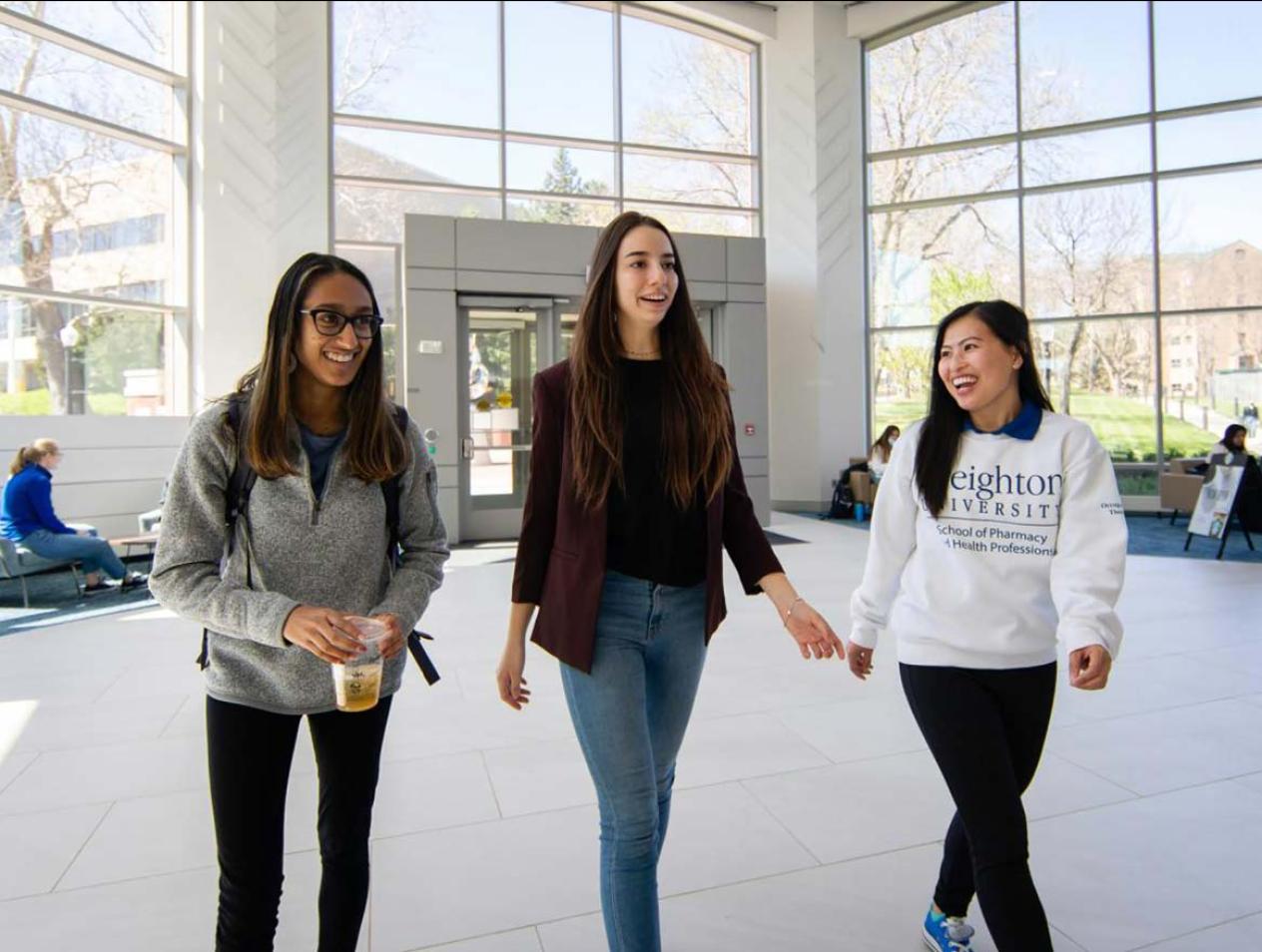 Three female Creighton students walking in Heider Business College entrance.