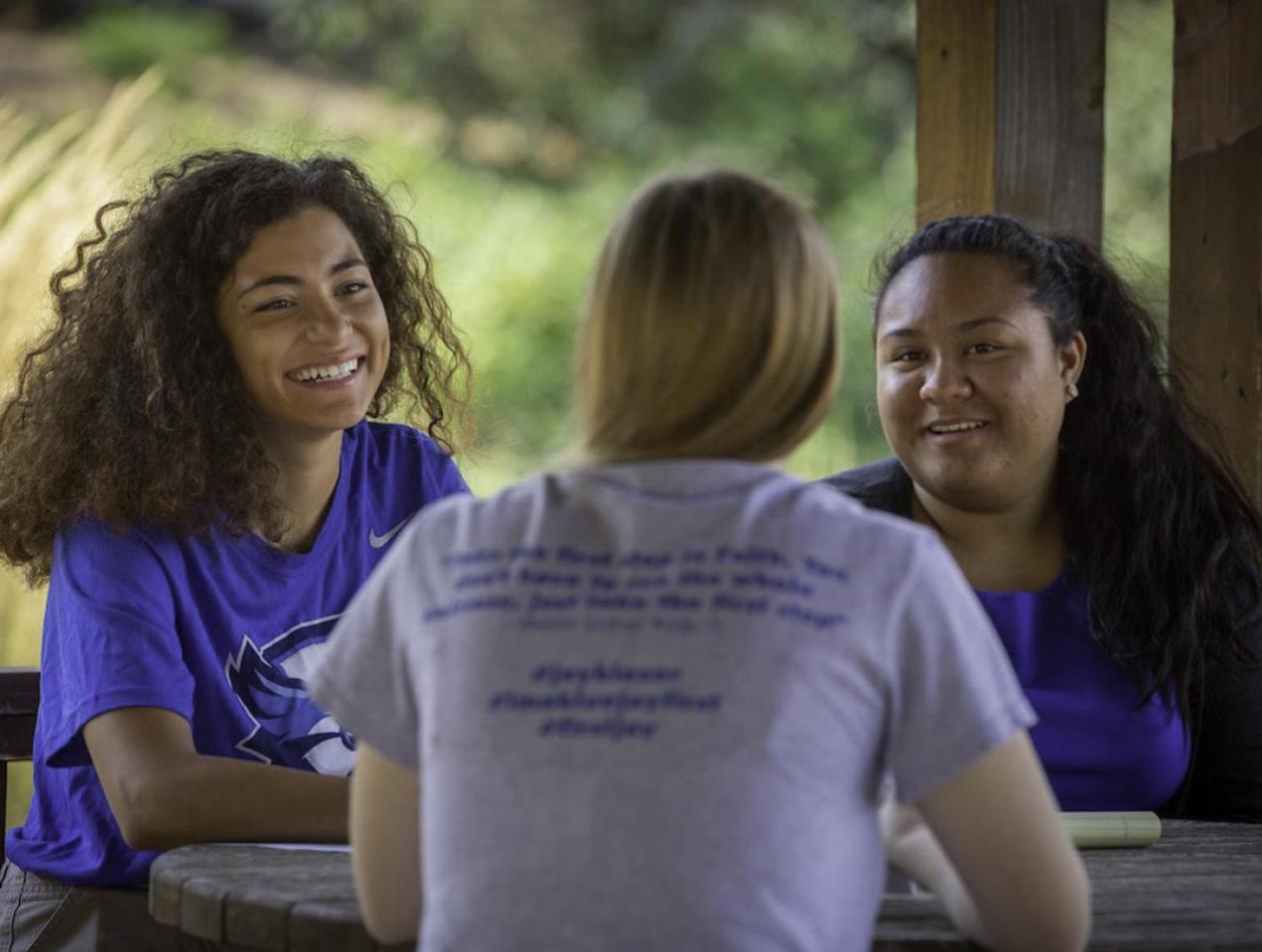 Female students smiling and talking at outdoor table