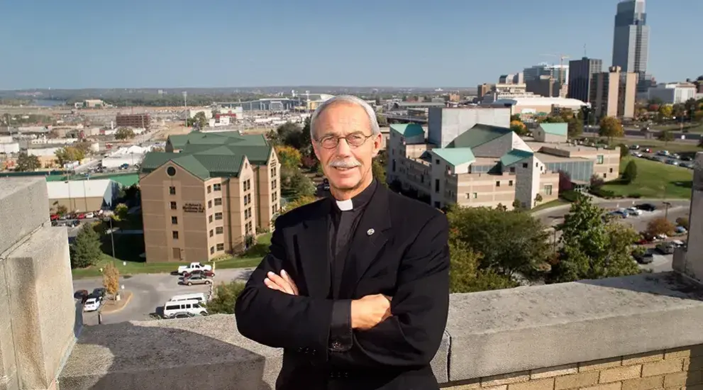 Father Schlegel standing atop building on Creighton with campus in background.