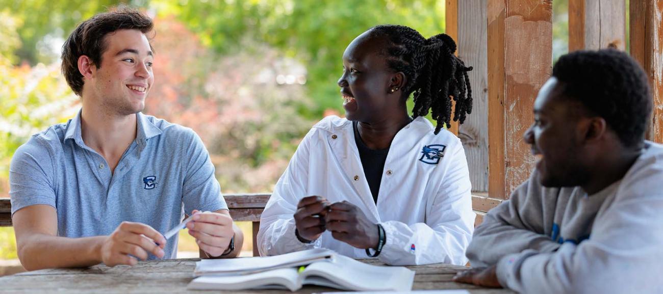 Three students smiling in white coats around a table