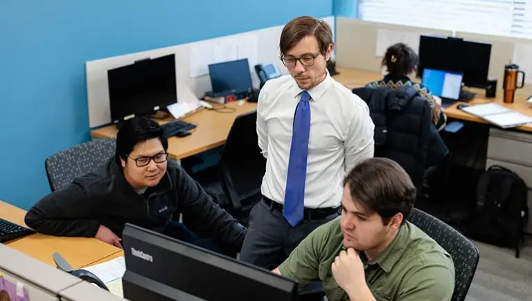 Three people strategizing around a computer.