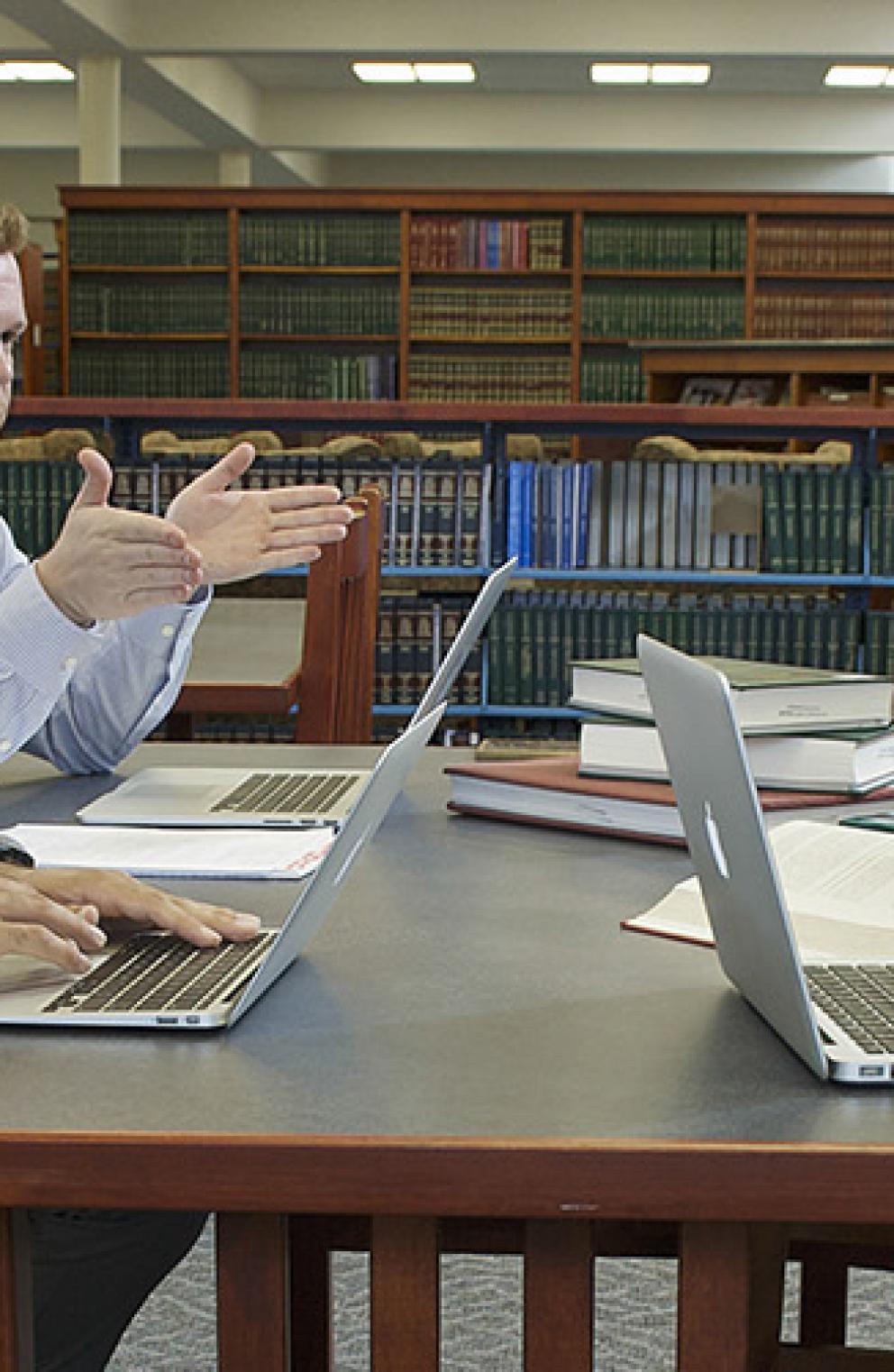 Two men talking at desk in law library