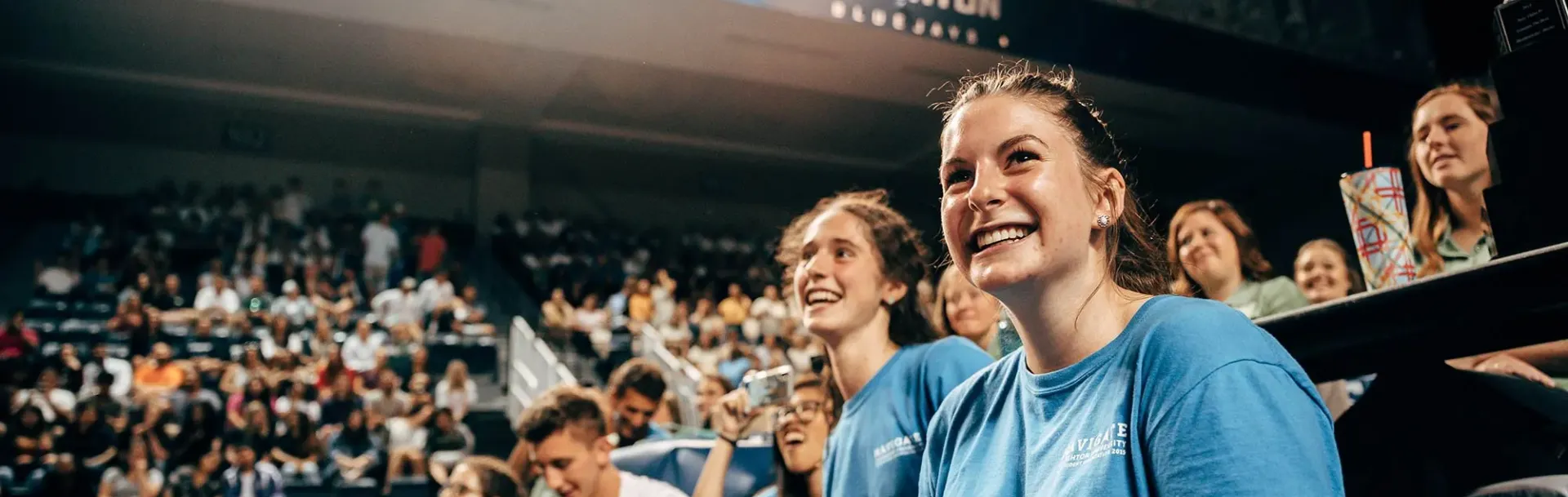 Smiling students in blue shirts watching a Creighton University event surrounded by a crowd.