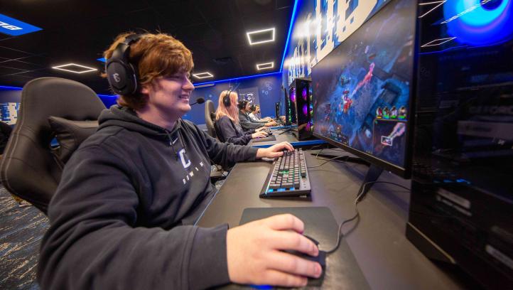 A student wearing a black sweatshirt sitting in a gaming room on Creighton's campus playing a video game on a computer.