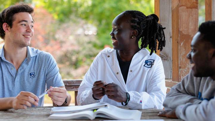 Three students smiling in white coats around a table