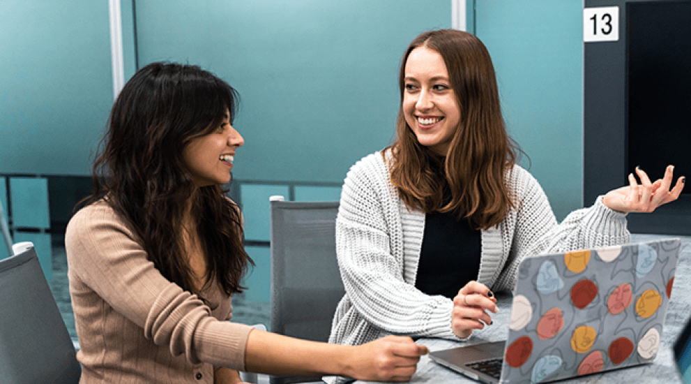 one white female student and one Indian female student talking