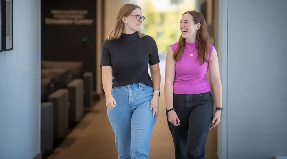 Two students walking and talking in hallway.