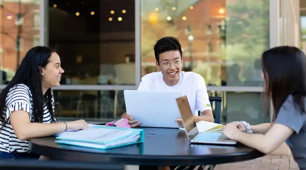 Three students smiling while studying at table.